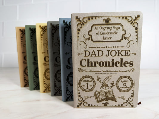 Dad Joke Chronicles laser engraved journal in light gray, sage green, light blue, beige, tan, and dark gray